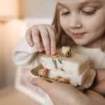 A smiling child appreciates a handcrafted soap with dried flowers in a warm, cozy setting.